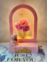 Pink rose arrangement inside arch frame with LED lights and teddy